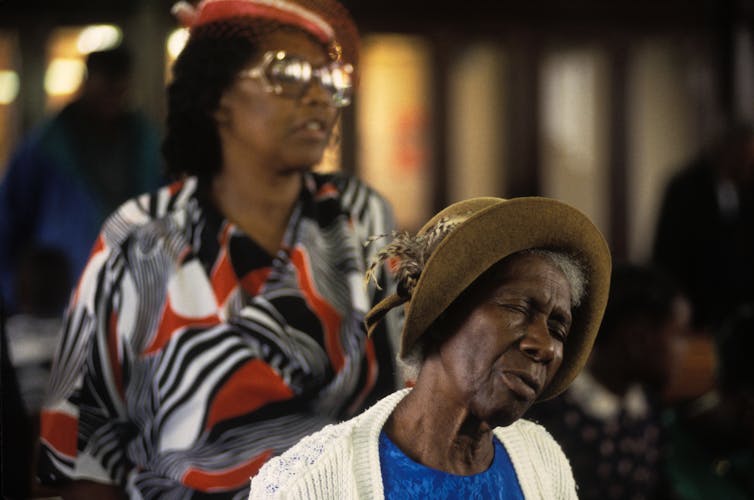 Two ladies in dresses and hats in church.