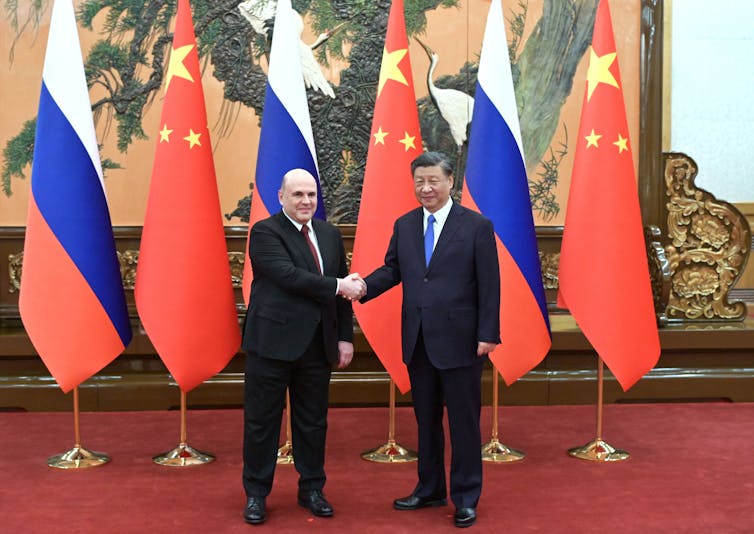 Two men shake hands in front of Russian and Chinese flags