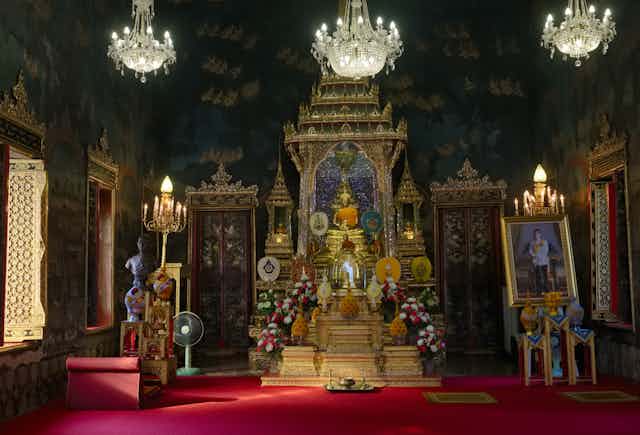 A Buddhist shrine in Bangkok, Thailand with a golden statue of the Buddha in the center and  a portrait of King Maha Vajiralongkorn (Rama X) on the right.