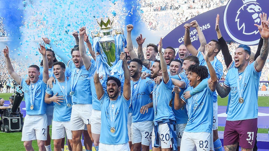 Manchester City in blue shirts holding the Premier League trophy aloft