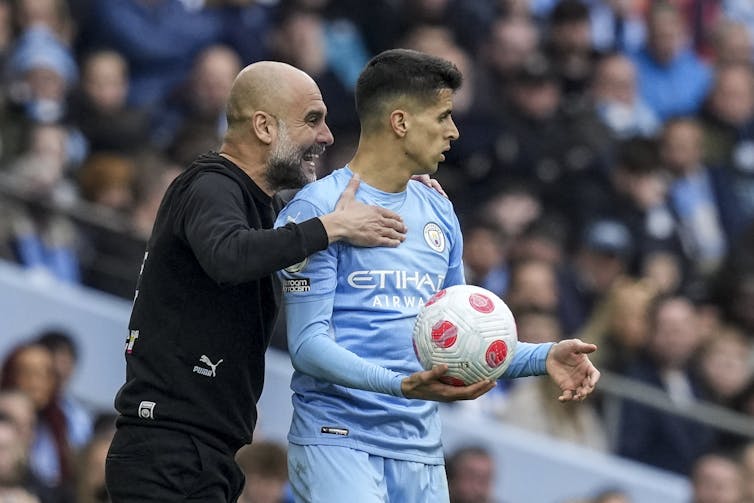 Pep Guardiola in black speaks to Joao Cancelo in his Man City kit in 2020.