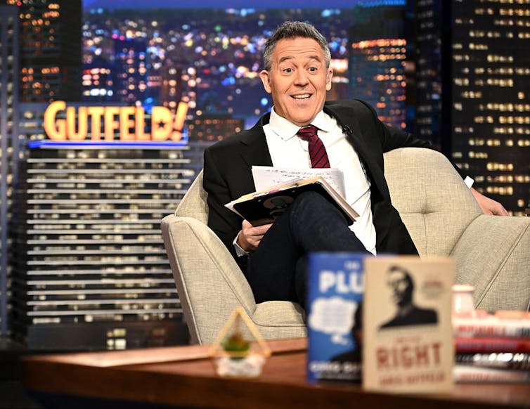 Man in suit sits in chair while grinning.