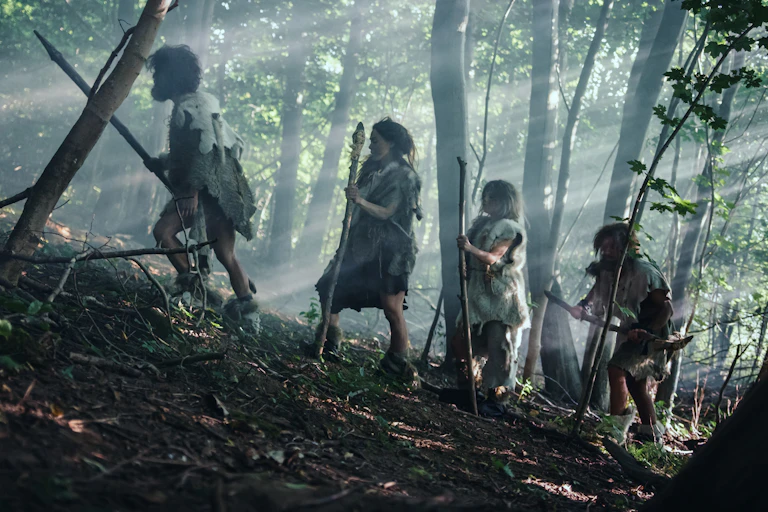 four people with spears wearing skins in woods