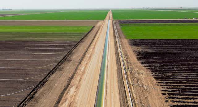A narrow canal stretches through green fields and darker plowed areas