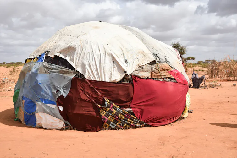 A tent composed of different coloured sheets and rope on dry, sandy ground.