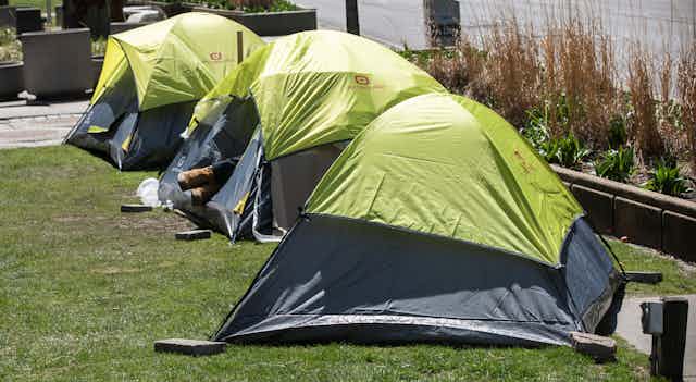 Three bright green tents are seen in a row, a person's feet sticking out of one of them.
