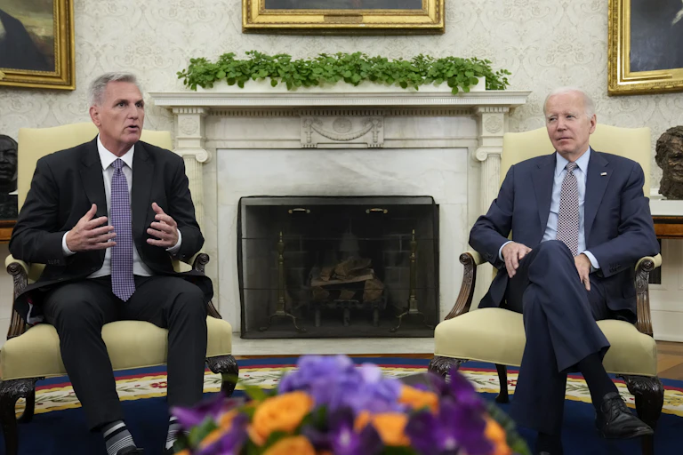 Two men sitting in yellow armchairs in front of an elegant fireplace.