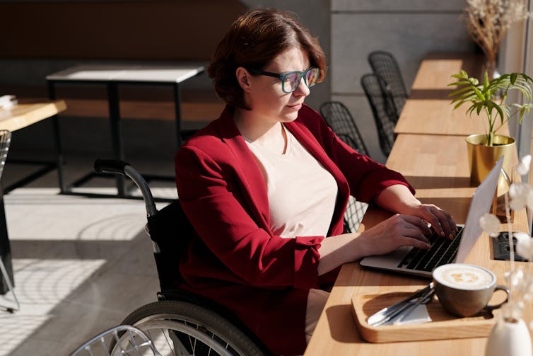 A woman in a wheelchair work on a laptop in a cafe.