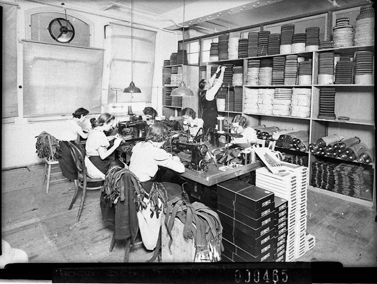 Women in the foreground machining as storeman stacks the finished articles in the rack