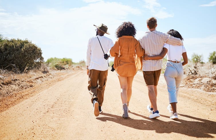 Four people arm in arm walking along dirt road