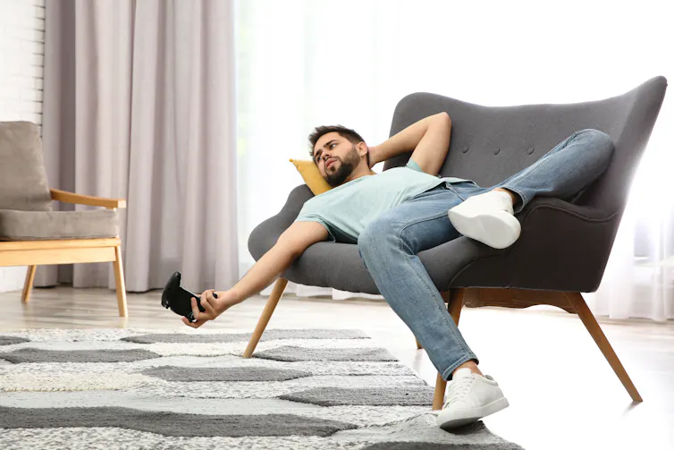 Man lays on his couch with a video game controller in his hand.