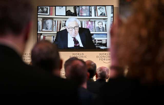 A roomful of people watch Henry Kissingger deliver an address at the Davos World Economic Forum.