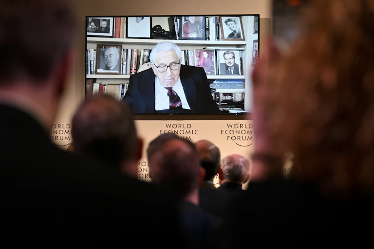 A roomful of people watch Henry Kissingger deliver an address at the Davos World Economic Forum.