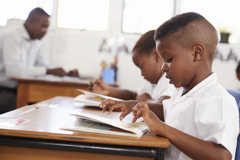 A boy in a school uniform uses his finger to track books in a book