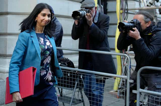 Home Secretary Suella Braverman, carrying a red minister's folder, walks past several photographers