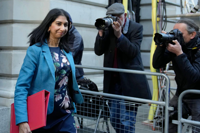 Home Secretary Suella Braverman, carrying a red minister's folder, walks past several photographers