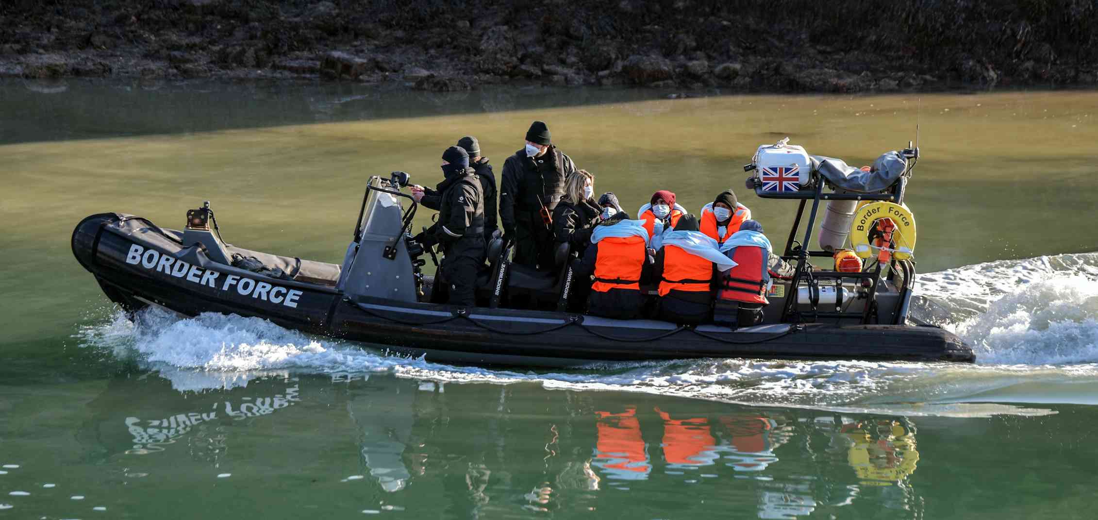 A Border Force boat carrying a small number of people in orange life vests.