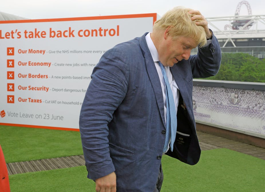Boris Johnson walking, with his hand on his head, in front of a sign that says 'let's take back control of our money, economy, borders, security and taxes'
