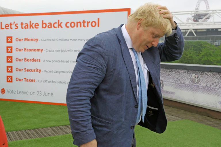 Boris Johnson walking, with his hand on his head, in front of a sign that says 'let's take back control of our money, economy, borders, security and taxes'