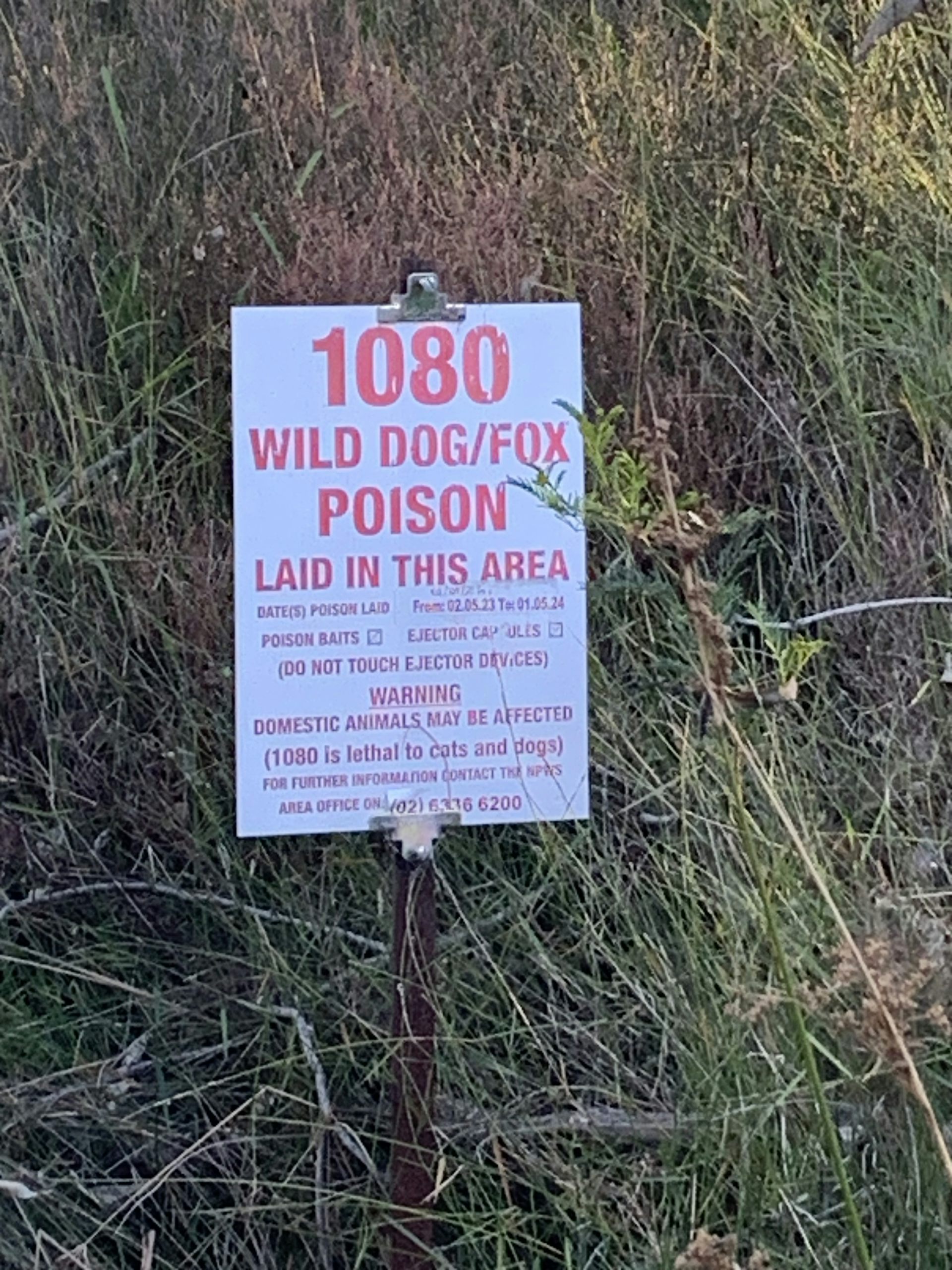 A white sign with red text stating that 1080 wild dog and fox poison baits are laid in the area.