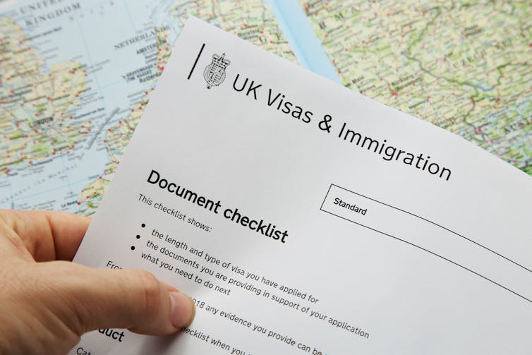 Close up of a person's hand holding a paper copy of a Uk Visas and immigration application, over a world map in the background