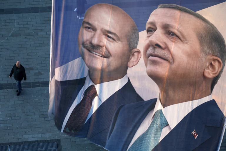 A flag shows the image of two men far above and man walking on the pavement.