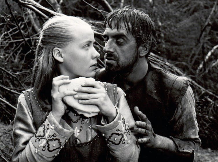 A woman dressed in medieval clothes eats while a man grabs her from behind.