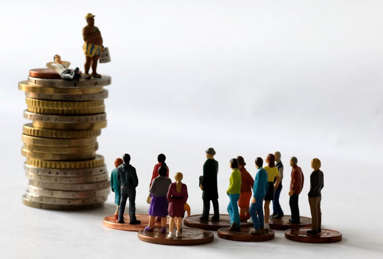 Tiny human figures standing on coins: a few people on a tall stack, and a lot of people on much smaller stacks