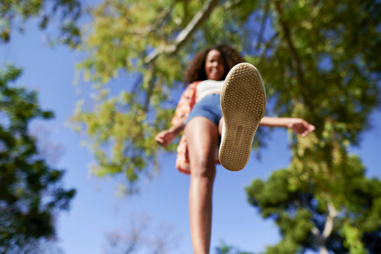Low angle shot of shoe sole of person walking beneath trees