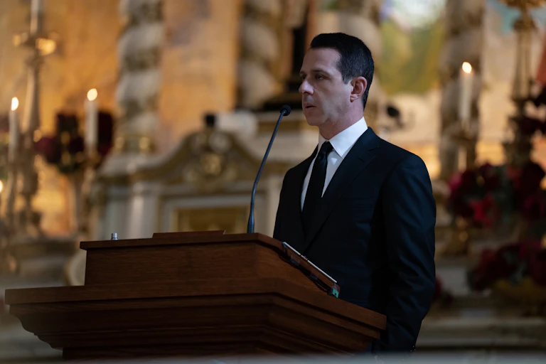 Kendall Roy (Jeremy Strong) stands behind a lectern in a black suit.