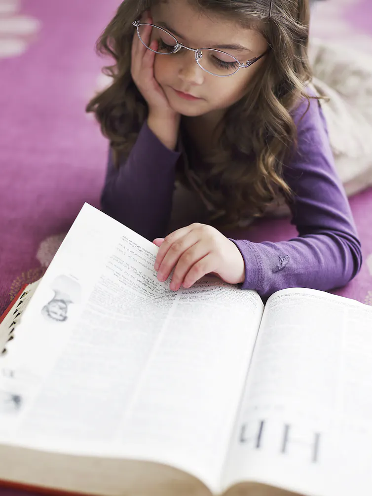 A girl reads a dictionary as she lies on the floor.