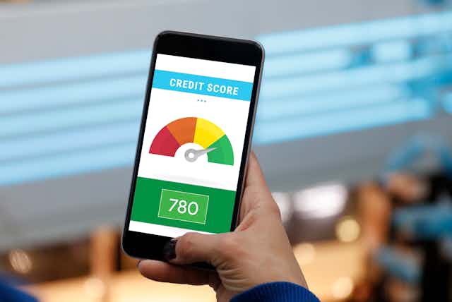 A man holds a smartphone showing an image of an individual's credit score in the green zone on a continuum from red to green..
