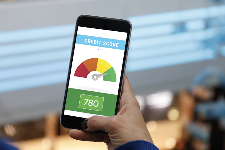 A man holds a smartphone showing an image of an individual's credit score in the green zone on a continuum from red to green..