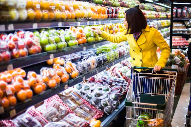 A young woman examines packaged fruit on a grocery store shelf