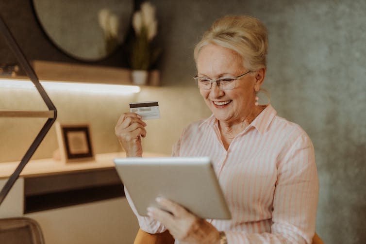 A smiling woman looks at her computer while holding a credit card in her right hand.