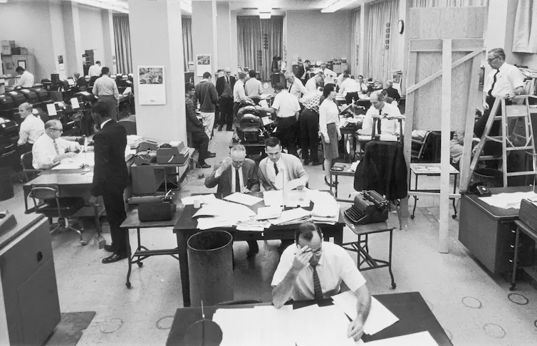 A black-and-white photo of journalists working in a newsroom