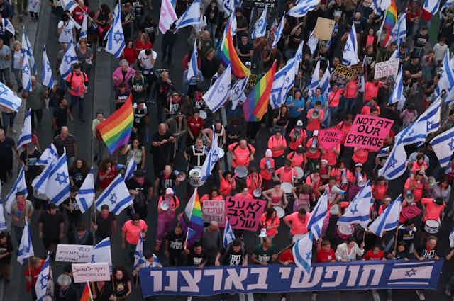 A scene of a protest, with Israeli flags and LGBTQ pride flags, viewed from above.