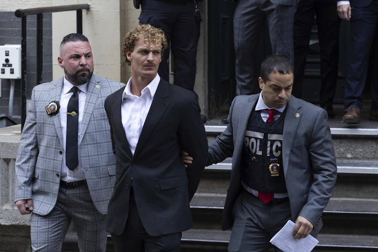 Two police officers escort a man with blond curly hair.