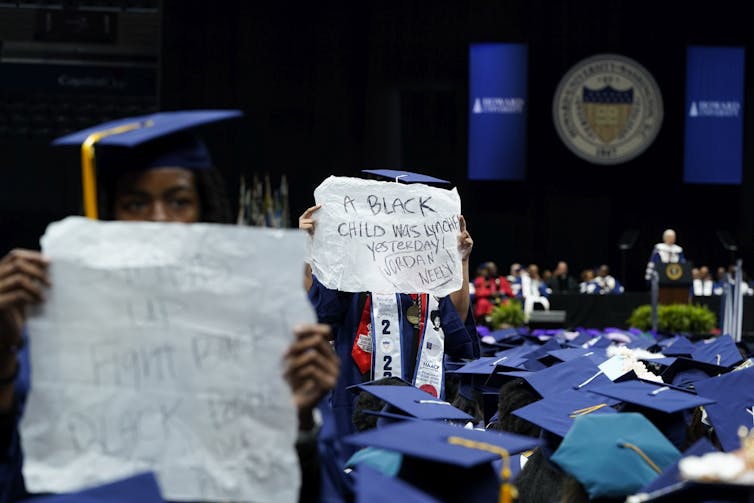 College graduates in blue robes hold up anti-racism signs.