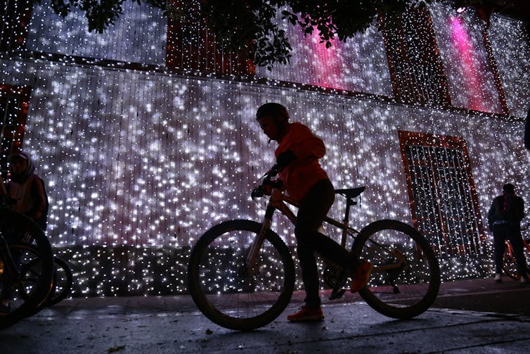 Person rides bike in front of hanging lights.