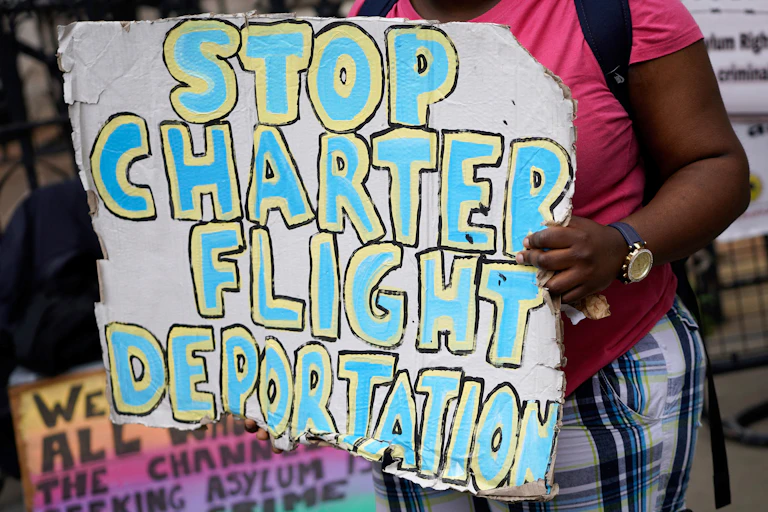 A woman holding a placard with the words 'stop charter flight deportation'.