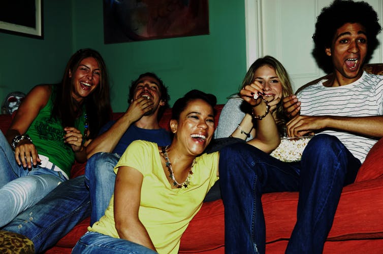 friends laughing together on couch watching out of frame TV
