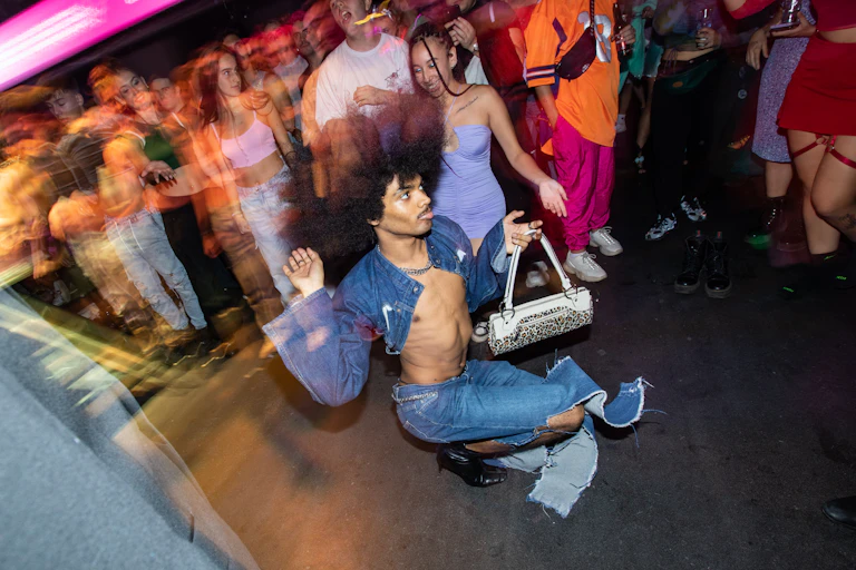 Person with afro holding purse dances on stage.