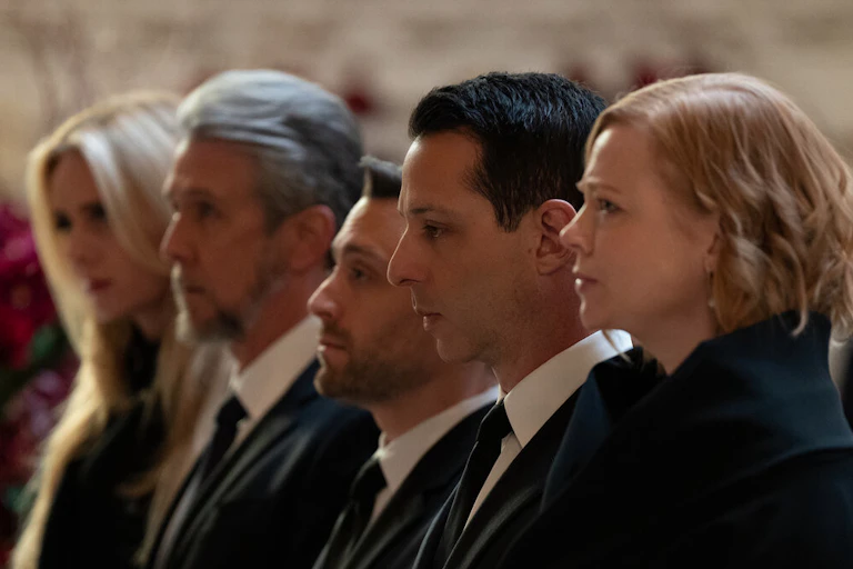 Three men and two women dressed in black stand at a funeral.