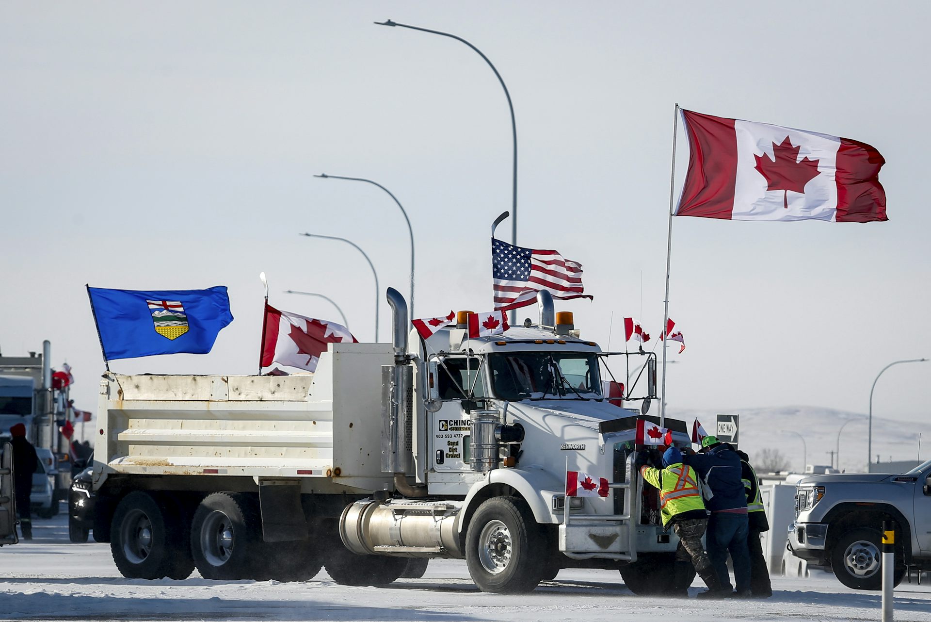 A large truck flying a Canadian, U.S. and Alberta flags is parked on a snowy road near the border.
