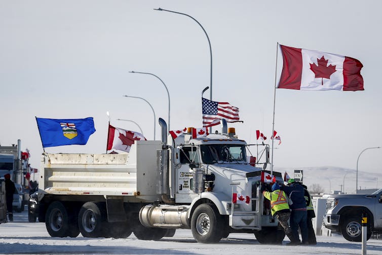 A large truck flying a Canadian, U.S. and Alberta flags is parked on a snowy road near the border.