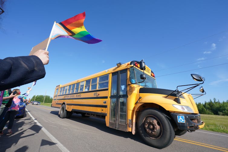 A pride flag seen flying near a school bus.