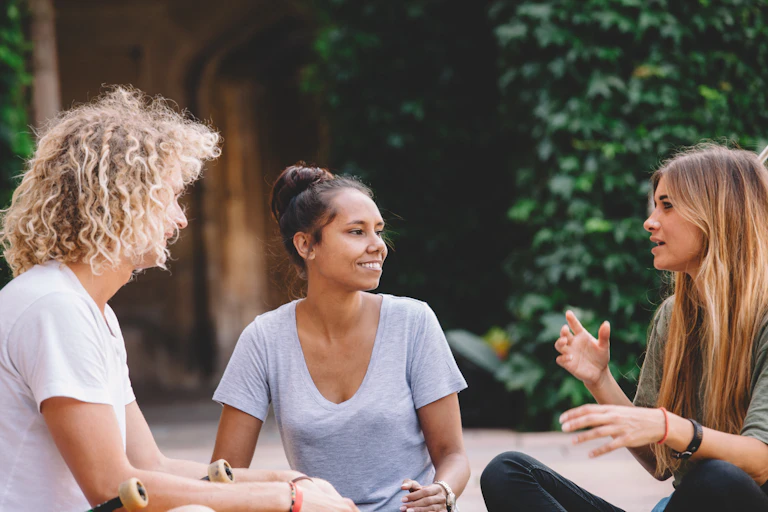 Three people sit on the ground talking.