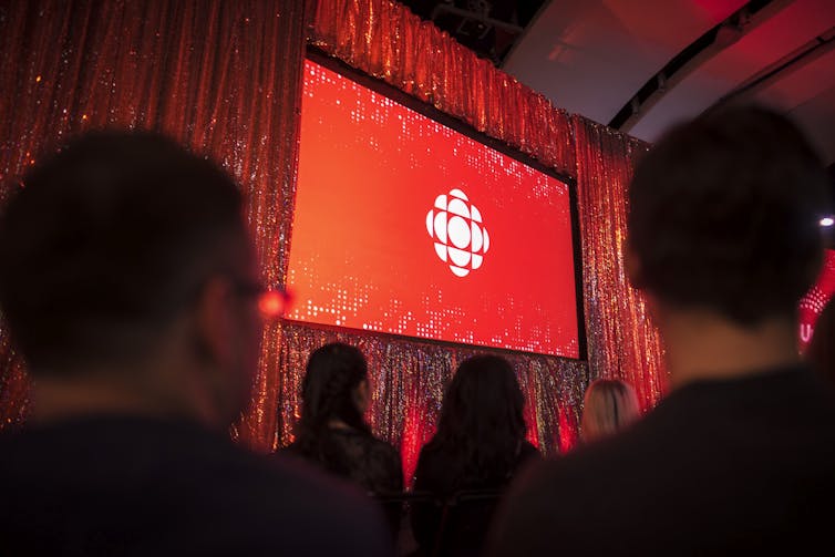 A red and white circular logo is projected on a screen.