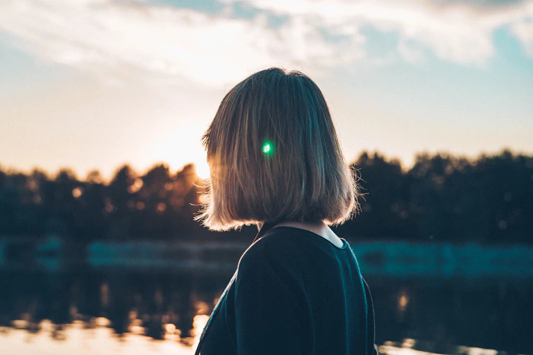 Woman looks at rising sun between trees
